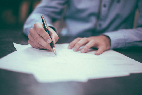 Close up of a persons hands as they write on some paper documents with a pen